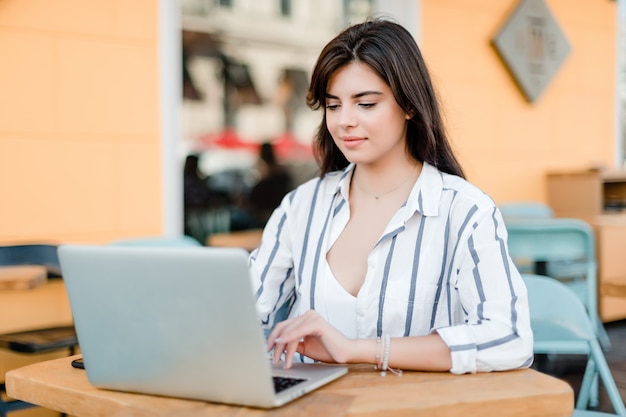 Femme souriante utilise un ordinateur portable assis près du café