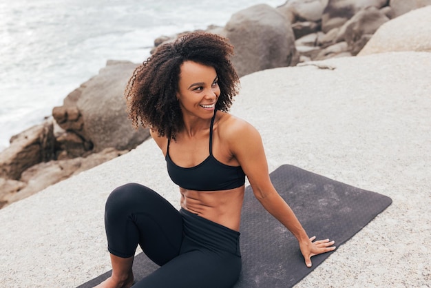 Une femme souriante en vêtements de sport se détend sur un tapis de yoga en regardant ailleurs