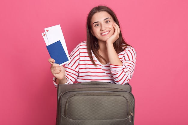 Femme souriante voyageur tenant un passeport avec billet posant avec valise,