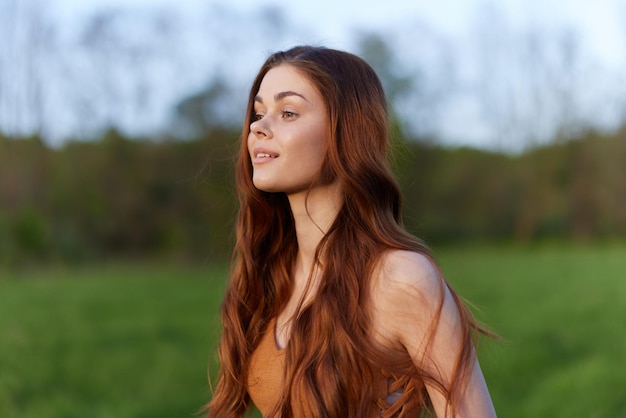 Une femme sourit et est heureuse dans la nature dans un parc verdoyant regarde le coucher du soleil et sourit Concept de mode de vie sain