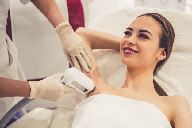 La femme sourit pendant que le médecin fait l’épilation au laser.