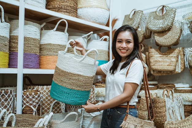 Femme sourit en soulevant un panier tressé debout parmi les objets d'artisanat dans la galerie d'artisanat