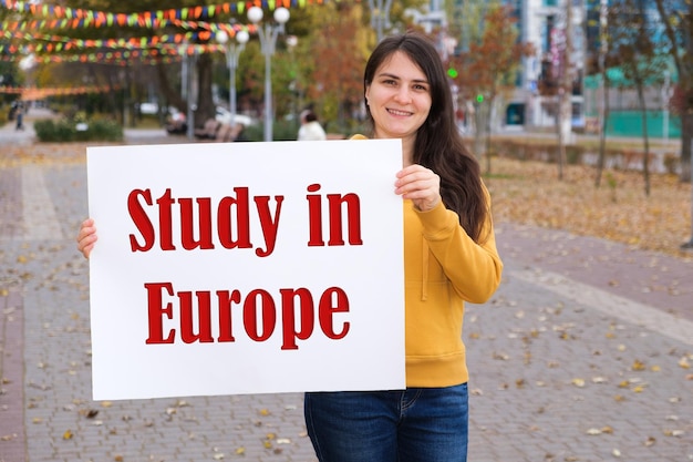 Une femme sourit et tient une affiche avec le texte Study in Europe