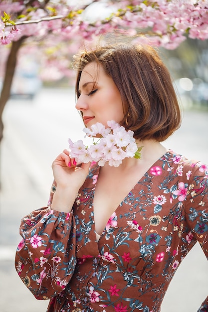 Une femme spectaculaire vêtue d'une robe brillante se dresse sur fond de sakura. Une femme brune dans une belle tenue sourit dans la rue en marchant