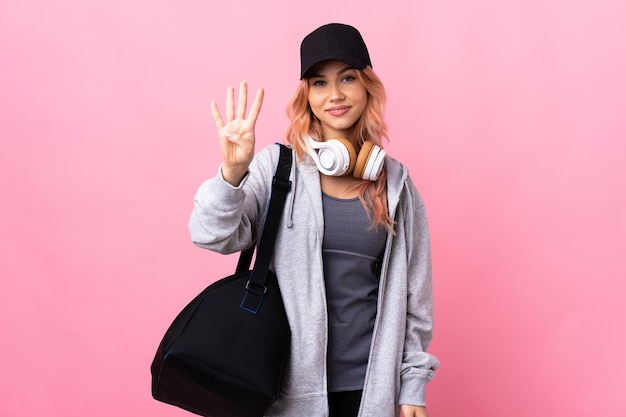 Femme de sport adolescent avec sac de sport sur mur isolé heureux et comptant quatre avec les doigts