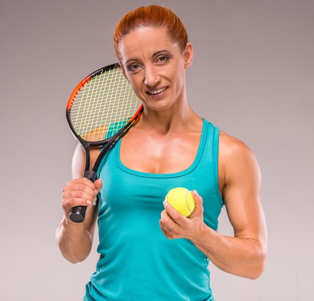Femme de sport d'âge moyen pose avec une raquette de tennis.