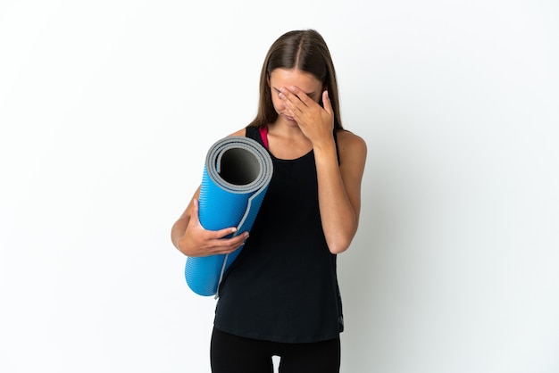 Femme de sport allant à des cours de yoga tout en tenant un tapis sur un mur blanc isolé avec une expression fatiguée et malade