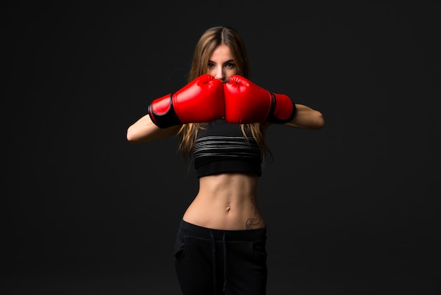 Femme de sport avec des gants de boxe sur fond sombre