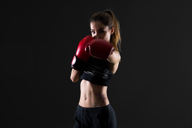 Femme de sport avec des gants de boxe sur fond sombre