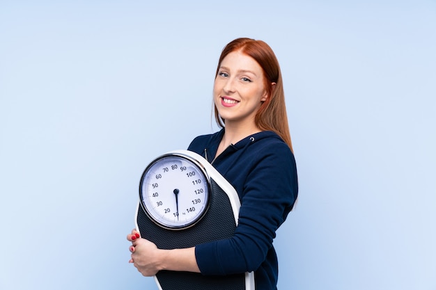 Femme sport jeune rousse sur fond bleu isolé avec machine de pesage