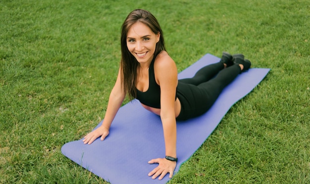 Femme de sport sain en tenue de sport faisant des exercices d'étirement allongé sur un tapis dans le parc
