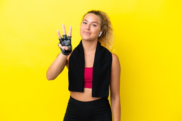 Femme de sport avec une serviette isolée sur fond jaune heureuse et comptant trois avec les doigts