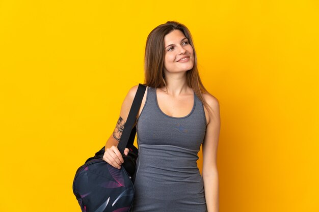 Femme de sport slovaque avec sac de sport isolé sur fond jaune à la recherche sur le côté et souriant