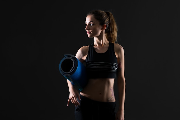 Femme de sport avec tapis sur fond sombre