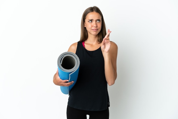 Femme sportive allant à des cours de yoga tout en tenant un tapis sur fond blanc isolé avec les doigts croisés et souhaitant le meilleur