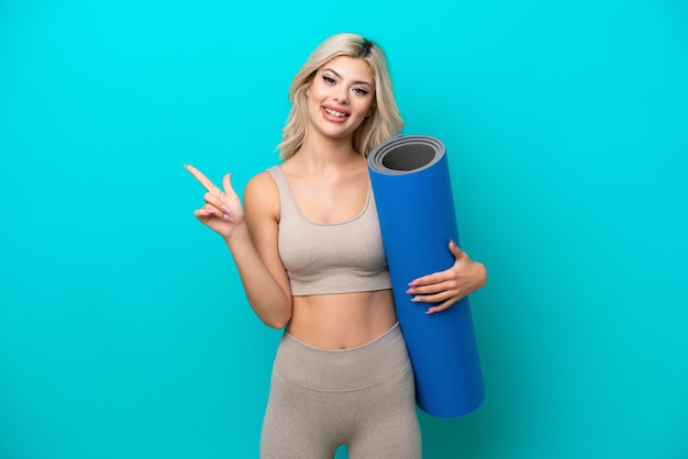 Femme sportive allant à des cours de yoga tout en tenant un tapis isolé sur fond bleu avec une expression faciale surprise