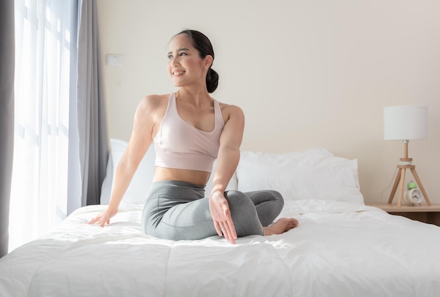 Femme sportive asiatique faisant de l'exercice de yoga et s'étirant après s'être réveillée le matin sur le lit à la maison