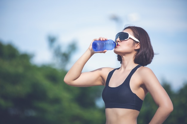 Femme sportive asin l'eau potable en plein air après avoir exécuté une journée ensoleillée