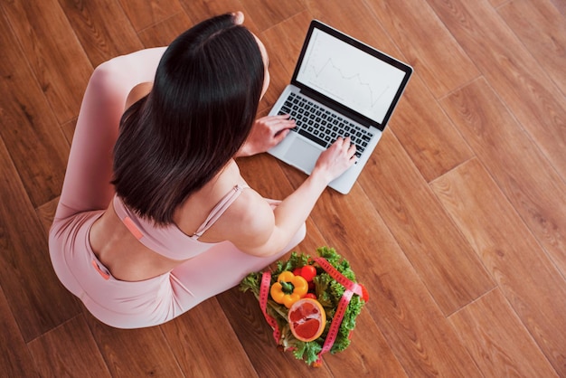 Femme sportive assise sur la table avec un ordinateur portable et des aliments sains.