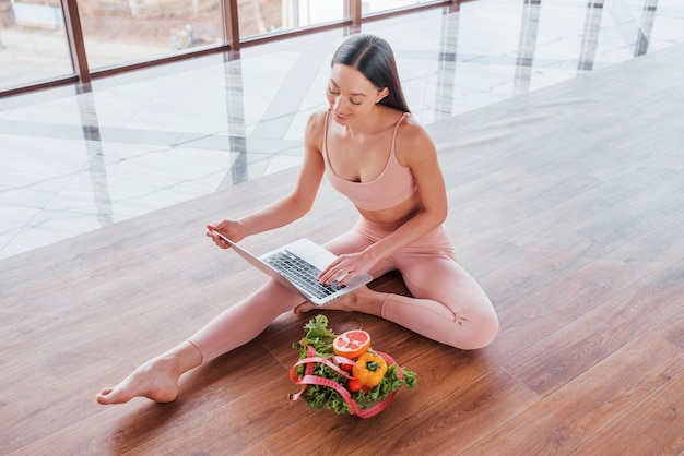 Femme sportive assise sur la table avec un ordinateur portable et des aliments sains.