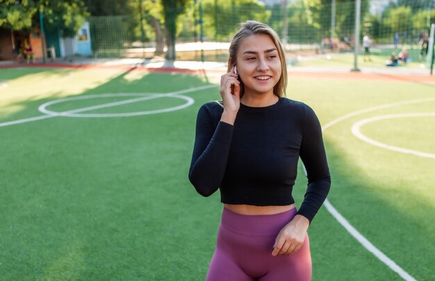 Femme sportive attrayante gaie écoutant de la musique avec des écouteurs à l'extérieur