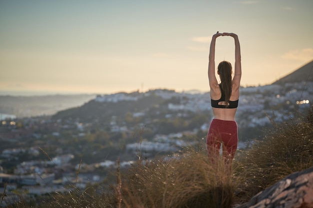 femme sportive aux cheveux longs et aux leggings rouges faisant du yoga au sommet de la montagne