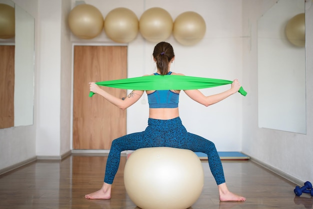 Femme sportive sur un ballon de fitness étend une vue arrière de bande élastique