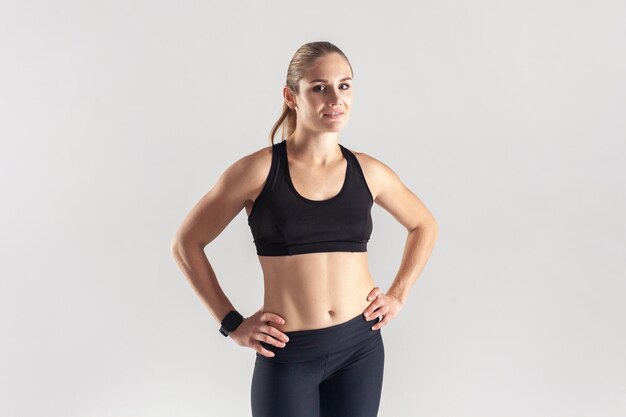 Une femme sportive confiante debout et regardant la caméra garde les mains sur les hanches posant après l'entraînement