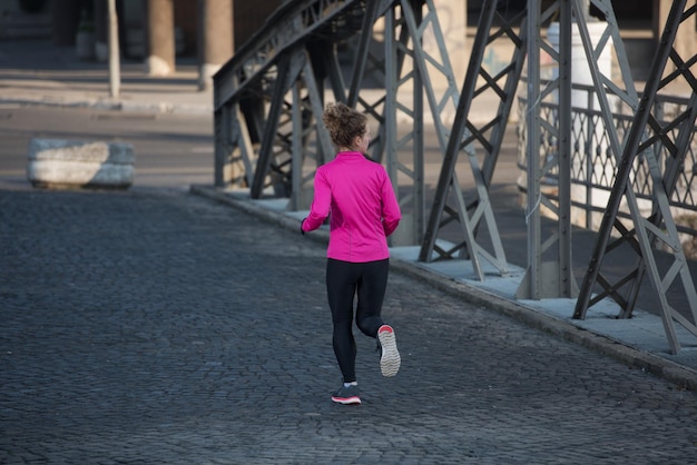 femme sportive courant sur le trottoir au jogging tôt le matin avec la scène du lever du soleil de la ville en arrière-plan