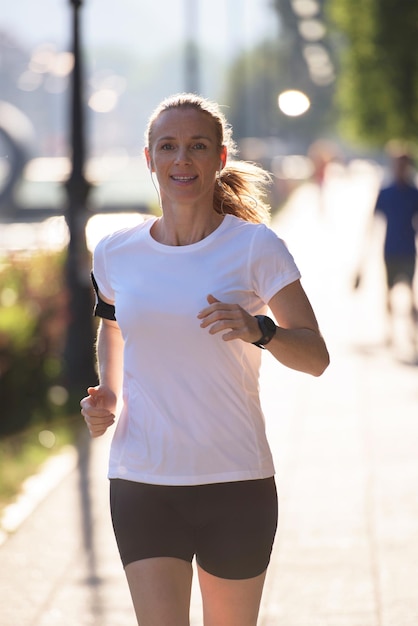 femme sportive courant sur le trottoir tôt le matin avec la scène du lever du soleil de la ville en arrière-plan