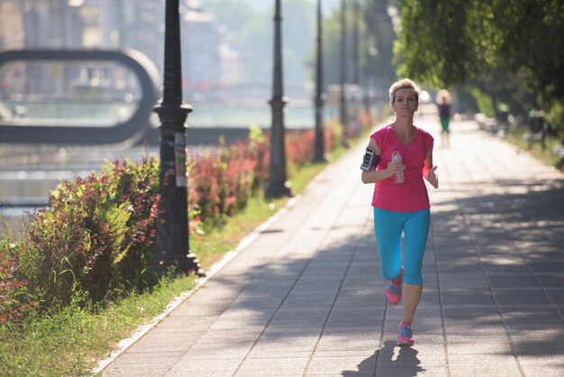 Photo femme sportive courant sur le trottoir tôt le matin avec la scène du lever du soleil de la ville en arrière-plan