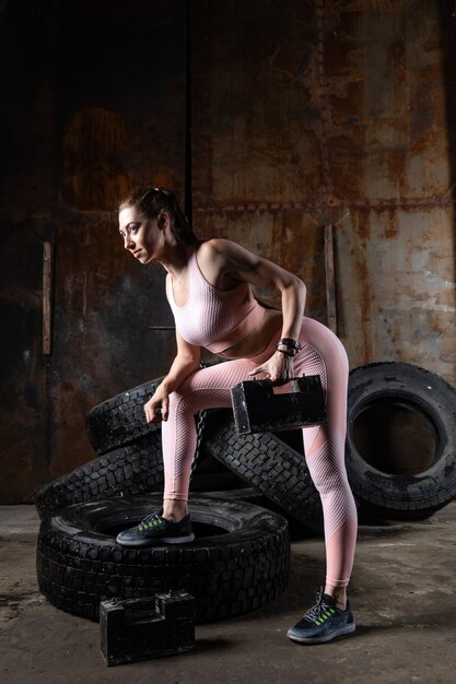 Femme Sportive Dans Un Haut Rose Et Leggings Faire De L'exercice Avec Des Haltères Sur Les Biceps Dans Le Garage De La Salle De Sport.