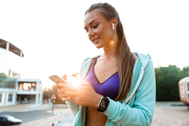 Femme sportive dans le parc en plein air, écouter de la musique avec des écouteurs à l'aide de téléphone mobile.