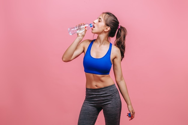 Femme sportive de l'eau potable sur le mur rose