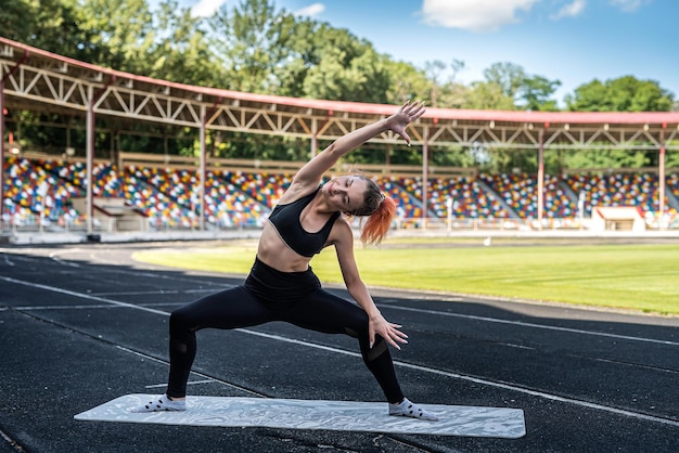 Femme sportive faisant des étirements ou des exercices de yoga sur le concept de flexibilité de la piste de course du stade