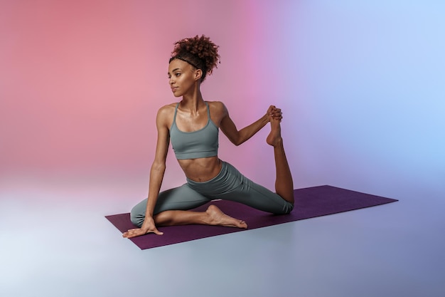 Femme sportive faisant des exercices d'étirement sur un tapis de yoga sur fond de studio avec filtre de couleur