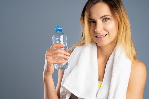 Femme sportive sur fond gris tenant une bouteille d'eau