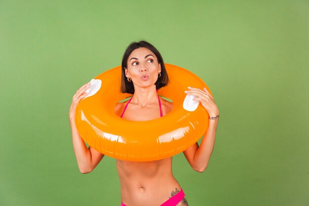 Femme sportive en forme d'été en bikini rose et anneau gonflable orange vif rond sur vert, joyeux joyeux excité joyeux positif