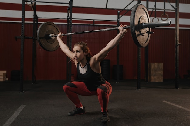 Femme sportive forte faisant des squats avec des barres lourdes au-dessus de la salle de gym