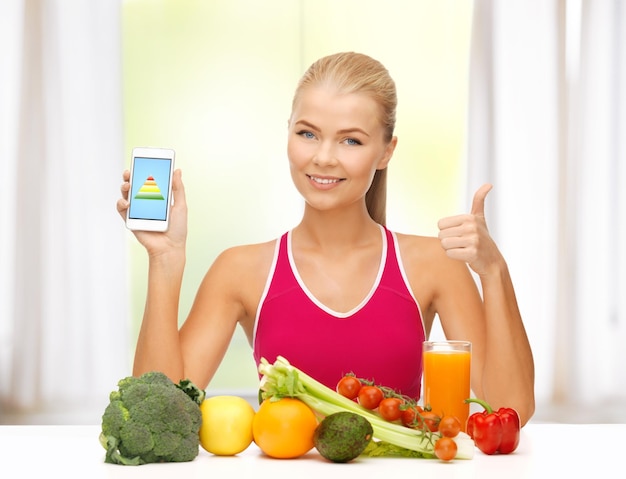 femme sportive avec des fruits et légumes montrant un smartphone