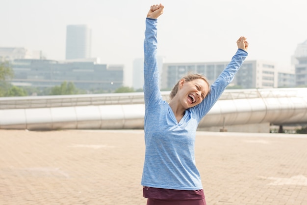 Femme sportive gaie, levant les mains dans la ville