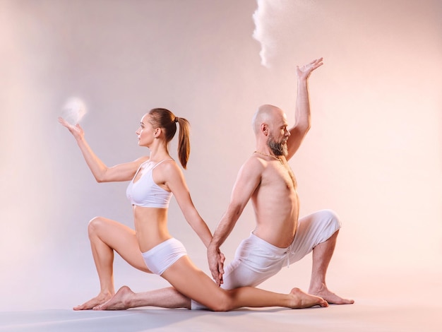 femme sportive et homme en vêtements blancs faisant des asanas de yoga avec du sable coloré à l'intérieur