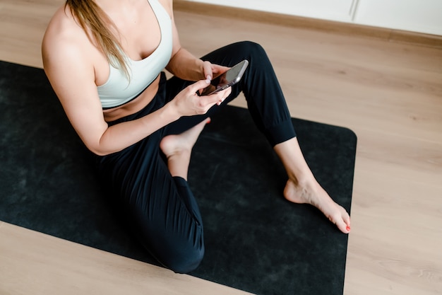 Femme sportive à la maison avec téléphone sur tapis de yoga