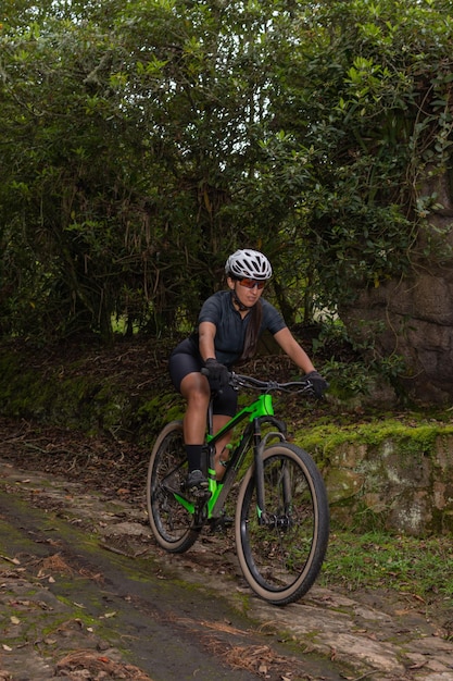 Femme sportive portant des lunettes et un casque faisant du vélo tout en descendant une montagne sur un chemin rustique