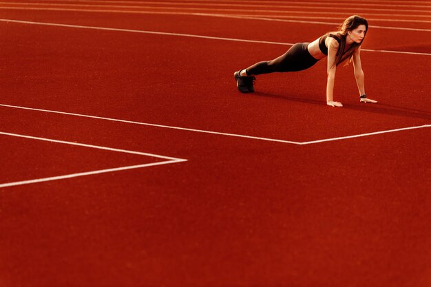 Femme sportive posant avec des muscles au stade faisant la flexibilité de la pratique d'étirement