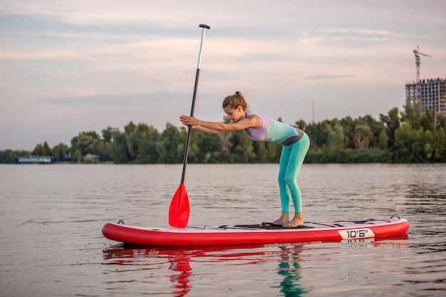 Femme sportive en position de yoga sur paddleboard, faisant du yoga sur sup board, exercice de flexibilité et étirement des muscles