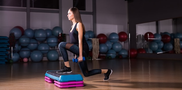 Femme sportive pratique sur plate-forme d'étape dans la salle de sport