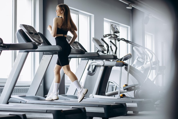 Femme sportive qui court sur tapis roulant à la salle de gym