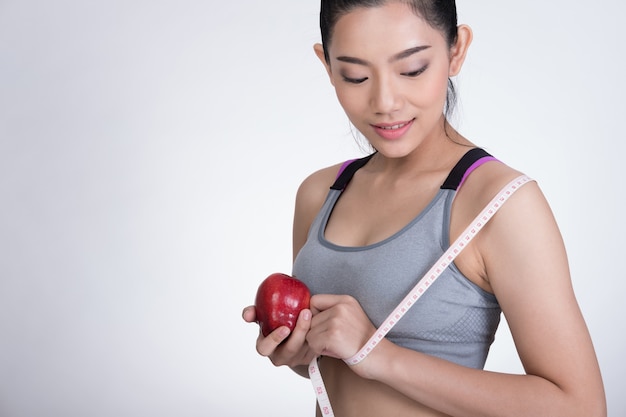 Femme sportive de remise en forme avec ruban à mesurer et pomme rouge debout contre le mur blanc