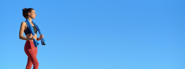 Femme sportive avec serviette et fond de ciel bleu ultra panoramique regardant sur le côté